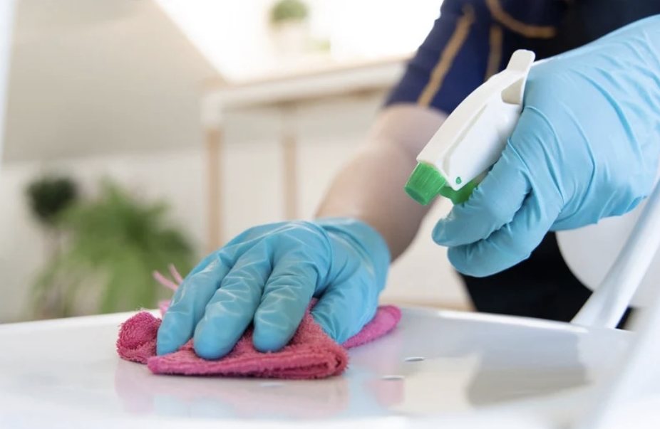 Mains gantées nettoyant une surface avec un spray et un chiffon